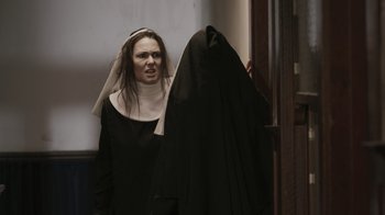 Movie still from “The Amityville Moon” (2021), directed by Thomas J. Churchill – A woman dressed up as a nun with a nun's head covering; Medium shot, Low angle