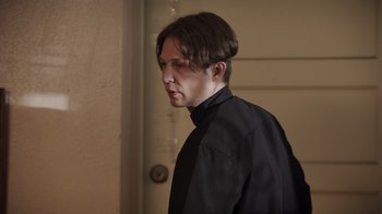 Movie still from “The Amityville Moon” (2021), directed by Thomas J. Churchill – A man wearing a black shirt and a black tie; Close Up shot, Low angle