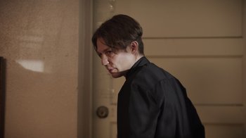 Movie still from “The Amityville Moon” (2021), directed by Thomas J. Churchill – A man in a black shirt is standing in a room; Close Up shot, Low angle