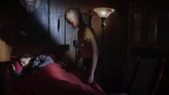 Movie still from “The Amityville Moon” (2021), directed by Thomas J. Churchill – A woman standing over a bed in a room; Wide shot, High angle