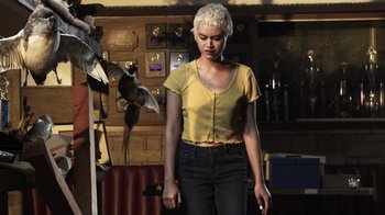 Movie still from “The Amityville Moon” (2021), directed by Thomas J. Churchill – A woman standing in front of a wall with a bird; Medium shot, Low angle