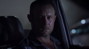 Movie still from “The Amityville Moon” (2021), directed by Thomas J. Churchill – A person sitting in a car at night; Close Up shot, Low angle