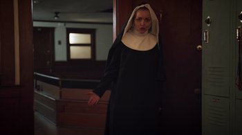 Movie still from “The Amityville Moon” (2021), directed by Thomas J. Churchill – A woman dressed as a nun standing in front of a door; Medium shot, Low angle