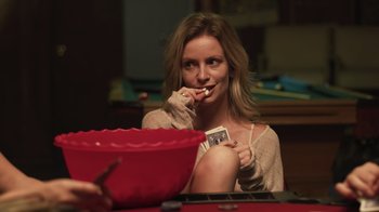 Movie still from “The Amityville Moon” (2021), directed by Thomas J. Churchill – A woman sitting at a table holding a card; Medium shot, Over the shoulder angle