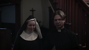 Movie still from “The Amityville Moon” (2021), directed by Thomas J. Churchill – A man and a woman dressed up as a priest and nun; Medium shot, Low angle