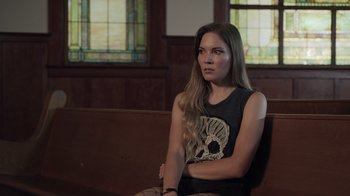 Movie still from “The Amityville Moon” (2021), directed by Thomas J. Churchill – A woman sitting on a bench in front of stained glass windows; Medium shot, Over the shoulder angle