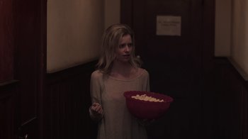 Movie still from “The Amityville Moon” (2021), directed by Thomas J. Churchill – A woman is holding a bowl of popcorn; Medium shot, Low angle