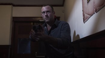 Movie still from “The Amityville Moon” (2021), directed by Thomas J. Churchill – A man in a dark room holding a gun; Medium shot, Low angle