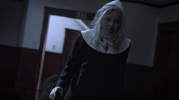 Movie still from “The Amityville Moon” (2021), directed by Thomas J. Churchill – A woman dressed up as a nun with blood on her face; Medium shot, Low angle