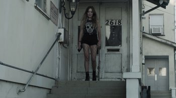 Movie still from “The Amityville Moon” (2021), directed by Thomas J. Churchill – A woman standing on the steps in front of a building; Wide shot, Low angle
