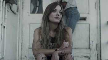 Movie still from “The Amityville Moon” (2021), directed by Thomas J. Churchill – A woman sitting on the steps of a building; Close Up shot, Low angle