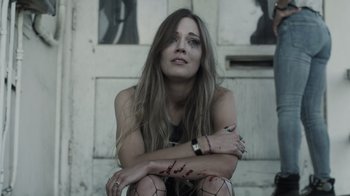 Movie still from “The Amityville Moon” (2021), directed by Thomas J. Churchill – A woman sitting on the ground with her arms crossed; Close Up shot, Low angle