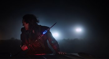 Movie still from “The Avengers” (2012), directed by Joss Whedon – A man holding a sword in the dark with lights in the background; Medium shot, Over the shoulder angle