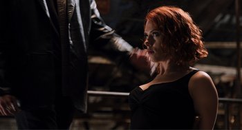 Movie still from “The Avengers” (2012), directed by Joss Whedon – A red headed woman in a black dress looking to her left; Medium shot, Over the shoulder angle