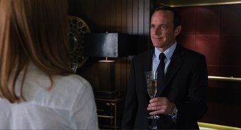 Movie still from “The Avengers” (2012), directed by Joss Whedon – A man in a suit holding a glass of champagne; Close Up shot, Over the shoulder angle