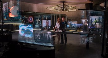 Movie still from “The Avengers” (2012), directed by Joss Whedon – Two people standing in front of a television set in a room; Wide shot, Over the shoulder angle