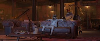 Movie still from “The Bad Guys” (2022), directed by Pierre Perifel – A man sitting on top of a couch next to a coffee table; Wide shot, Over the shoulder angle