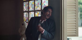 Movie still from “The Big 4” (2022), directed by Timo Tjahjanto – A man wearing a suit and tie standing in front of a window; Medium shot, Low angle