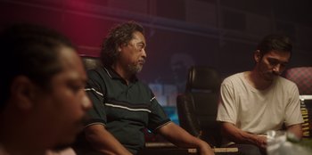 Movie still from “The Big 4” (2022), directed by Timo Tjahjanto – A man sitting on a chair in a room; Medium shot, Low angle