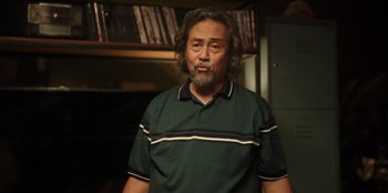 Movie still from “The Big 4” (2022), directed by Timo Tjahjanto – An older man in a green shirt is standing in front of a bookshelf; Close Up shot, Low angle