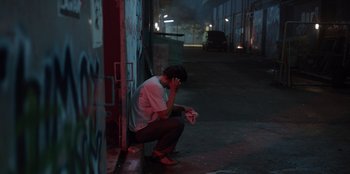 Movie still from “The Big 4” (2022), directed by Timo Tjahjanto – A man sitting on the side of the street holding a phone; Wide shot, High angle
