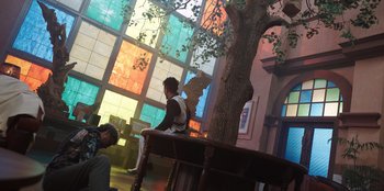 Movie still from “The Big 4” (2022), directed by Timo Tjahjanto – A boy sitting on a chair in a room with stained glass windows; Extreme Wide shot, Low angle