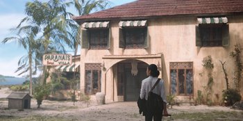 Movie still from “The Big 4” (2022), directed by Timo Tjahjanto – A woman standing in front of a building with palm trees in the background; Wide shot, Low angle