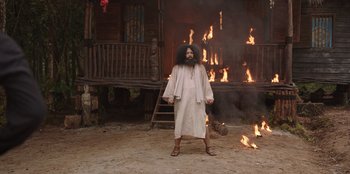 Movie still from “The Big 4” (2022), directed by Timo Tjahjanto – A man with a long beard standing in front of a burning house; Wide shot, Low angle