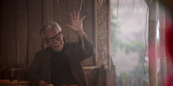 Movie still from “The Big 4” (2022), directed by Timo Tjahjanto – An old man with a beard and glasses smiling and waving; Medium shot, Low angle