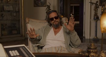 Movie still from “The Big Lebowski” (1998), directed by Ethan Coen – A man sitting in a chair holding his hands up; Medium shot, High angle