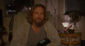 Movie still from “The Big Lebowski” (1998), directed by Ethan Coen – A man with long hair and beard sitting in a chair; Medium shot, Over the shoulder angle