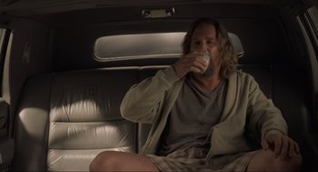 Movie still from “The Big Lebowski” (1998), directed by Ethan Coen – A man sitting in the back of a car drinking a beverage; Medium shot, Over the shoulder angle
