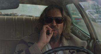 Movie still from “The Big Lebowski” (1998), directed by Ethan Coen – A man sitting in the drivers seat of a car smoking a cigarette; Medium shot, Low angle