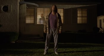 Movie still from “The Big Lebowski” (1998), directed by Ethan Coen – A man standing in the grass in front of a building; Wide shot, Low angle