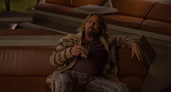 Movie still from “The Big Lebowski” (1998), directed by Ethan Coen – A man sitting on a couch holding a glass of wine; Medium shot, Low angle