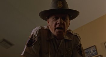Movie still from “The Big Lebowski” (1998), directed by Ethan Coen – A man in a hat and a uniform is sitting in a room; Close Up shot, Low angle