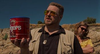 Movie still from “The Big Lebowski” (1998), directed by Ethan Coen – A man with a beard wearing sunglasses and holding a drink; Medium shot, Low angle