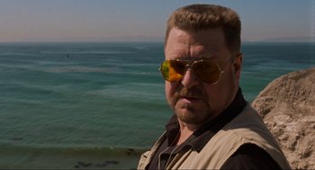Movie still from “The Big Lebowski” (1998), directed by Ethan Coen – A person wearing sunglasses near a body of water; Close Up shot, Low angle