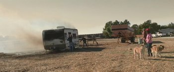 Movie still from “The Biggest Little Farm: The Return” (2022), directed by John Chester – Two men working on a trailer that has been set on fire; Extreme Wide shot, Low angle