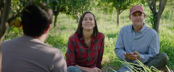 Movie still from “The Biggest Little Farm: The Return” (2022), directed by John Chester – A woman sitting on the ground in the grass; Medium shot, Over the shoulder angle