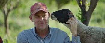 Movie still from “The Biggest Little Farm: The Return” (2022), directed by John Chester – A man with a hat and a cow's head; Close Up shot, Over the shoulder angle
