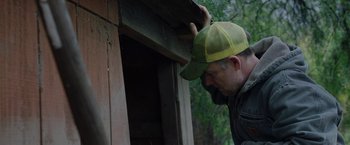 Movie still from “The Biggest Little Farm: The Return” (2022), directed by John Chester – A man wearing a hat leaning against a wooden structure; Medium shot, Low angle