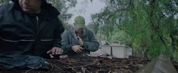 Movie still from “The Biggest Little Farm: The Return” (2022), directed by John Chester – A man wearing a green hat is cutting branches; Medium shot, Low angle