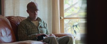 Movie still from “The Biggest Little Farm: The Return” (2022), directed by John Chester – A man sitting on top of a couch with a cat; Close Up shot, High angle