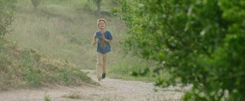 Movie still from “The Biggest Little Farm: The Return” (2022), directed by John Chester – A young boy running down a dirt road; Wide shot, High angle