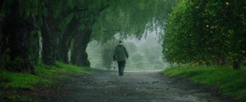 Movie still from “The Biggest Little Farm: The Return” (2022), directed by John Chester – A man walking down a path in the rain; Wide shot, Low angle