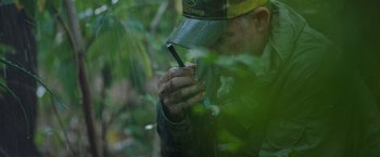 Movie still from “The Biggest Little Farm: The Return” (2022), directed by John Chester – A man with a hat on looking at a cell phone; Extreme Close Up shot, High angle