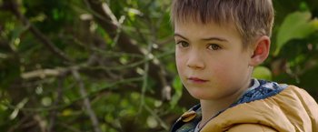 Movie still from “The Biggest Little Farm: The Return” (2022), directed by John Chester – A young boy's face with trees in the background; Close Up shot, Over the shoulder angle