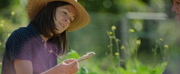 Movie still from “The Biggest Little Farm: The Return” (2022), directed by John Chester – A woman in a straw hat holding a piece of food; Close Up shot, Low angle