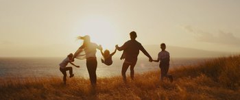 Movie still from “The Binge” (2020), directed by Jeremy Garelick – A group of people running in the grass near the water; Wide shot, Low angle